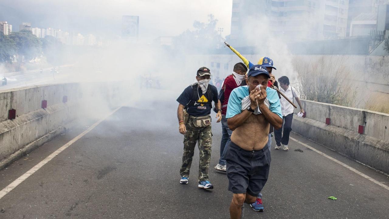 Demonstranten bedecken sich den Mund zum Schutz vom Tränengas bei einem Protest gegen die Regierung von Präsidenten Maduro. Demonstranten bedecken sich den Mund zum Schutz vom Tränengas bei einem Protest gegen die Regierung von Präsidenten Maduro.