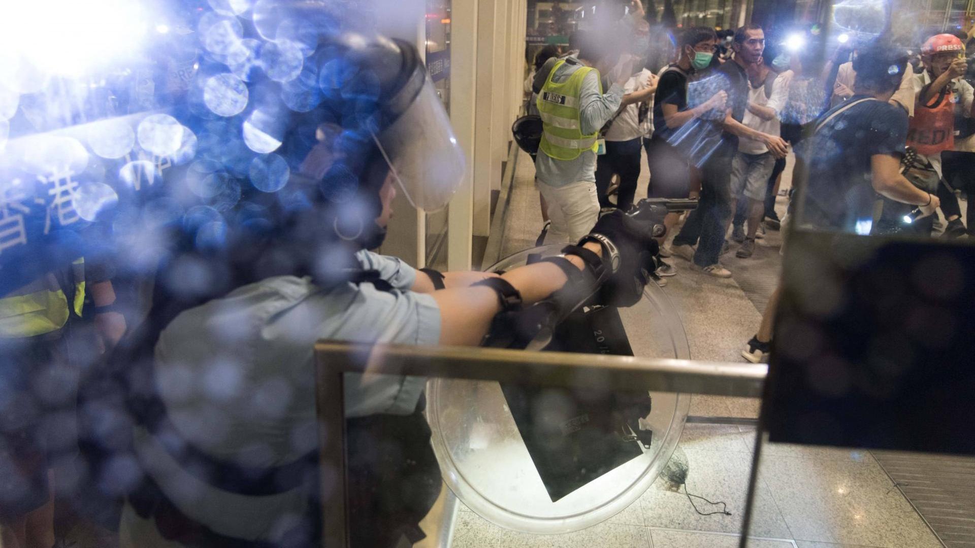 Dramatische, unübersichtliche Szene eines Polizisten, der seine Waffe in einem Terminal auf einen Aktivisten richtet Dramatische, unübersichtliche Szene eines Polizisten, der seine Waffe in einem Terminal auf einen Aktivisten richtet