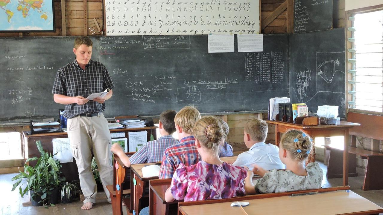 Eine Schulklasse sitzt auf Holzbänken vor Lehrer und Tafel. Eine Schulklasse sitzt auf Holzbänken vor Lehrer und Tafel.