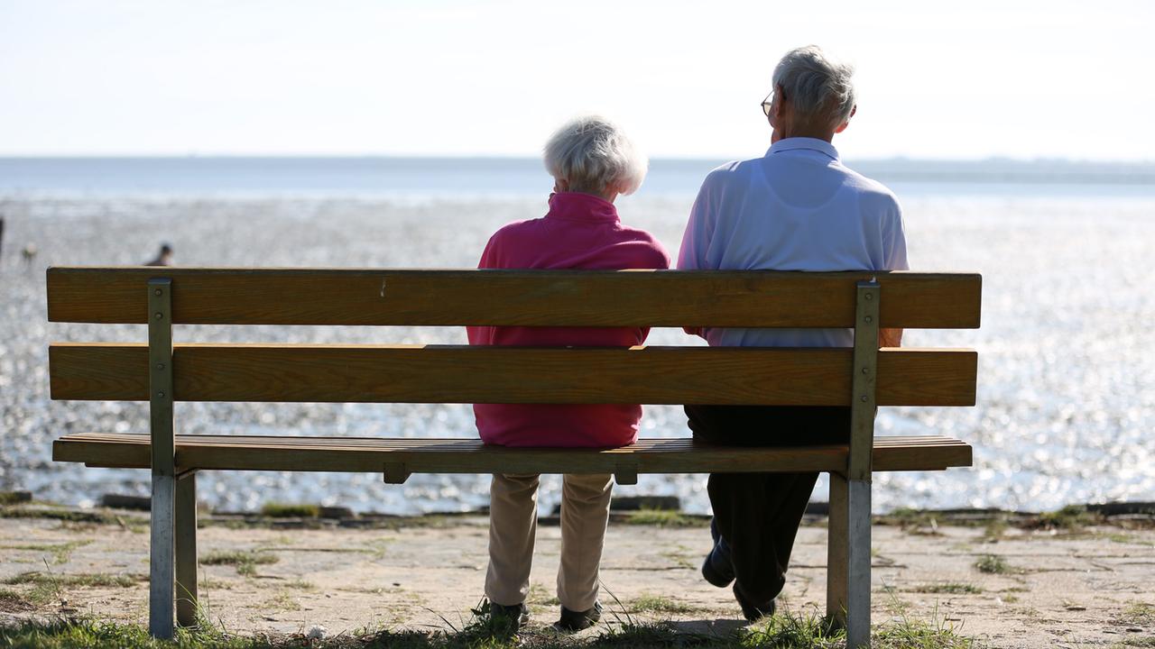 Ein Senioren-Paar sitzt auf einer Bank und schaut auf das im Watt.