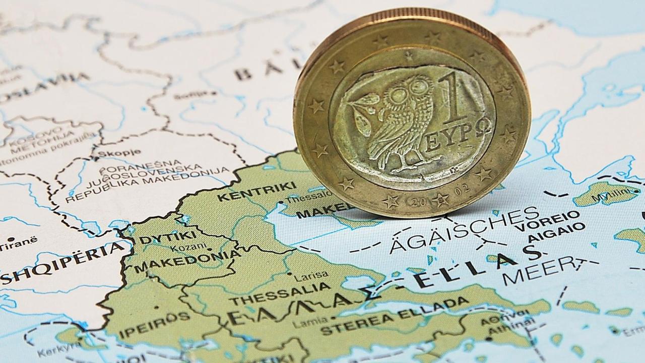Eine griechische Euro-Münze steht hochkant auf einer Landkarte Griechenlands. Eine griechische Euro-Münze steht hochkant auf einer Landkarte Griechenlands.