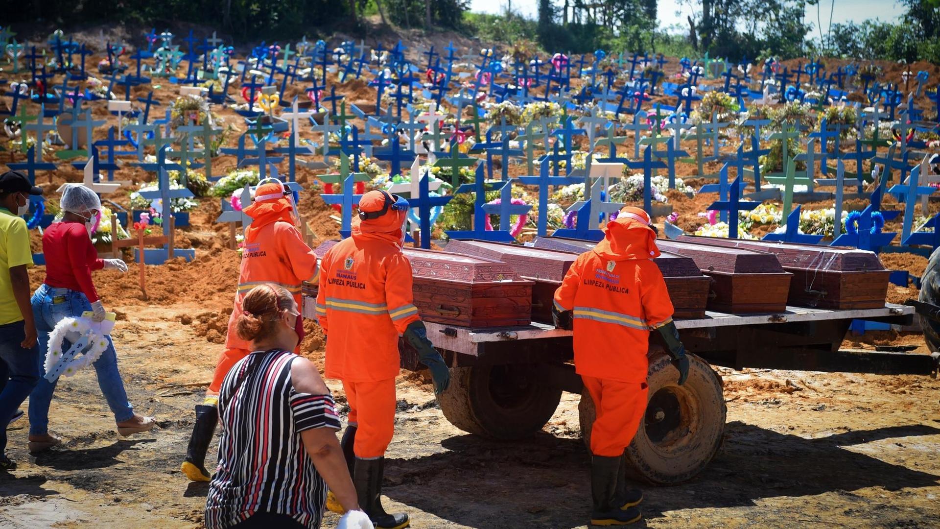 Brasilien, Manaus: Friedhofsmitarbeiter, gefolgt von Angehörigen der Toten mit Mundschutzmasken, fahren Särge zu einem Massengrab. Angesichts der steigenden Zahl von Corona-Infektionen ist das Gesundheitswesen in Manaus am Limit.