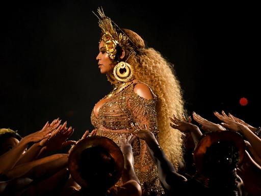 Das Bild zeigt die Musikerin Beyoncé bei einem Konzert vor buntem Effektnebel. Der Podcast "Making Beyoncé" porträtiert die Künstlerin in drei Episoden.