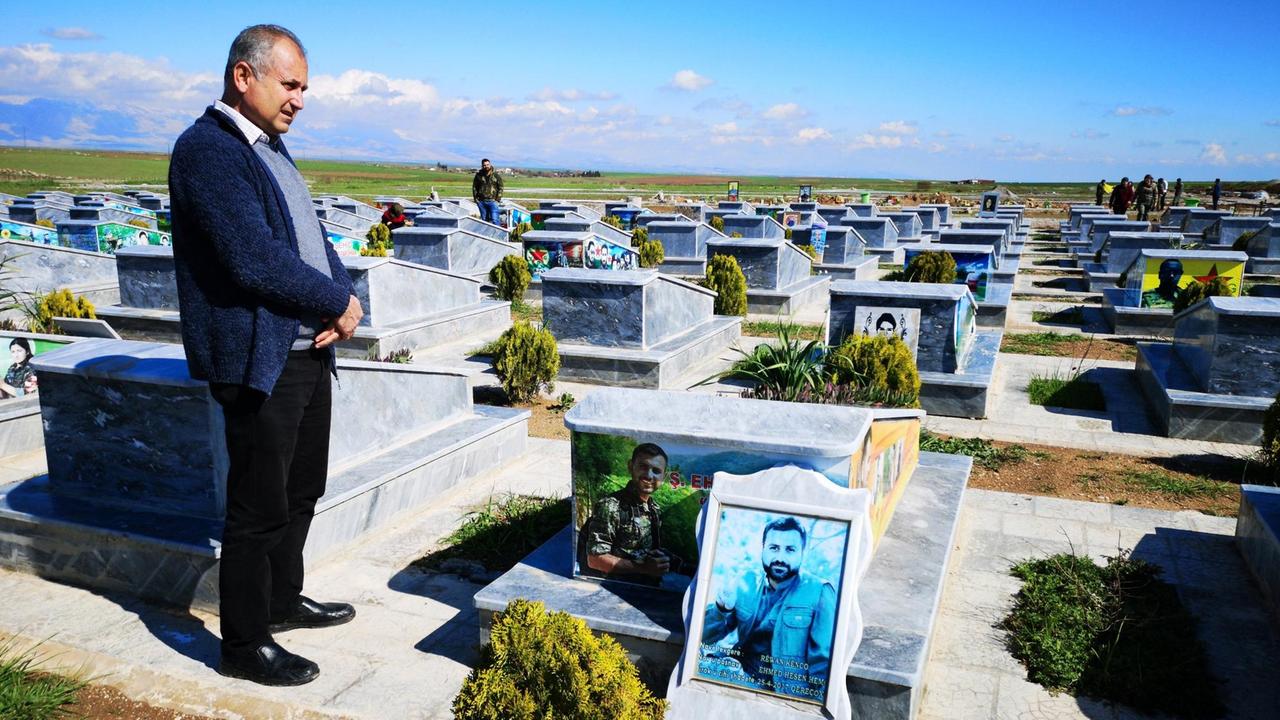 Der Friedhof der Märtyrer bei Dêrik. Ein Mann steht nebenb einem Grab. Die Grabplatten sind aus Marmor und reihen sich wie Dominosteine in langen Reihen aneinander.