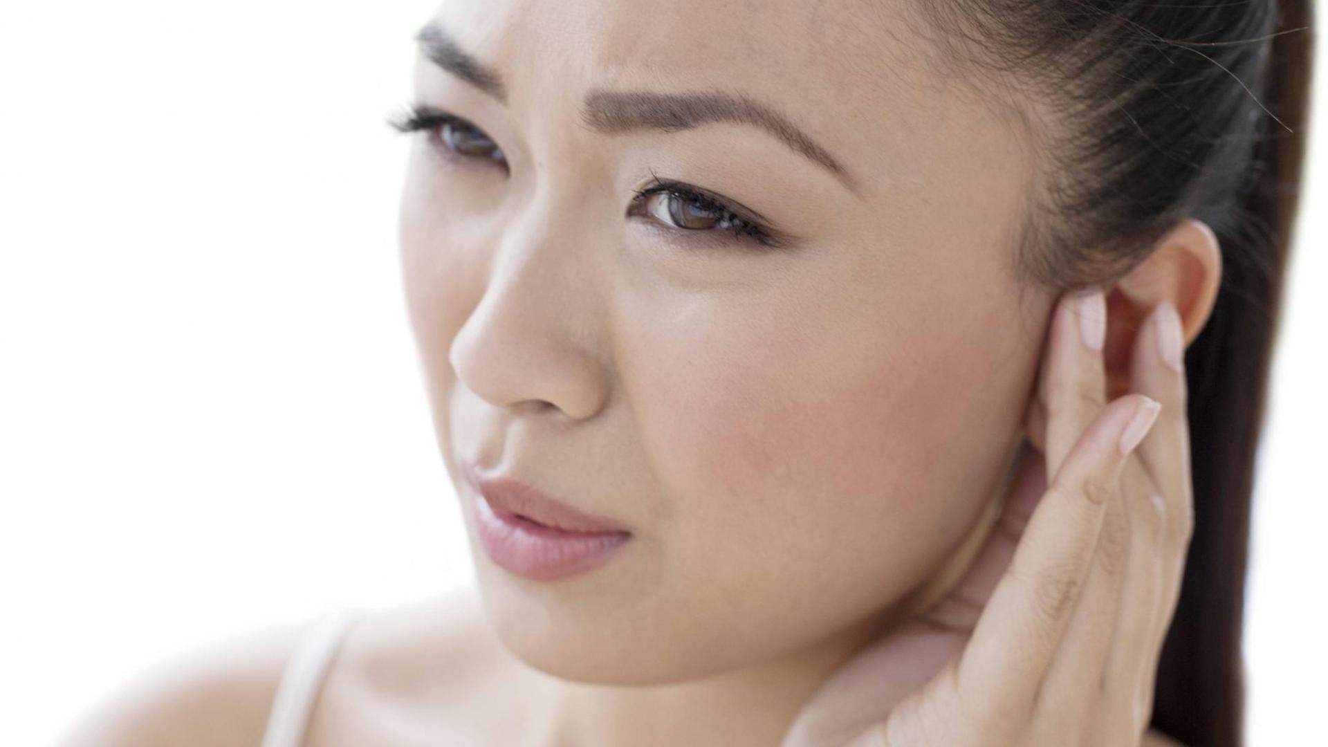 Tinnitus kann irritierend und auch schmerzhaft sein - eine Frau fasst sich schmerzerfüllt an ihr linkes Ohr Tinnitus kann irritierend und auch schmerzhaft sein - eine Frau fasst sich schmerzerfüllt an ihr linkes Ohr