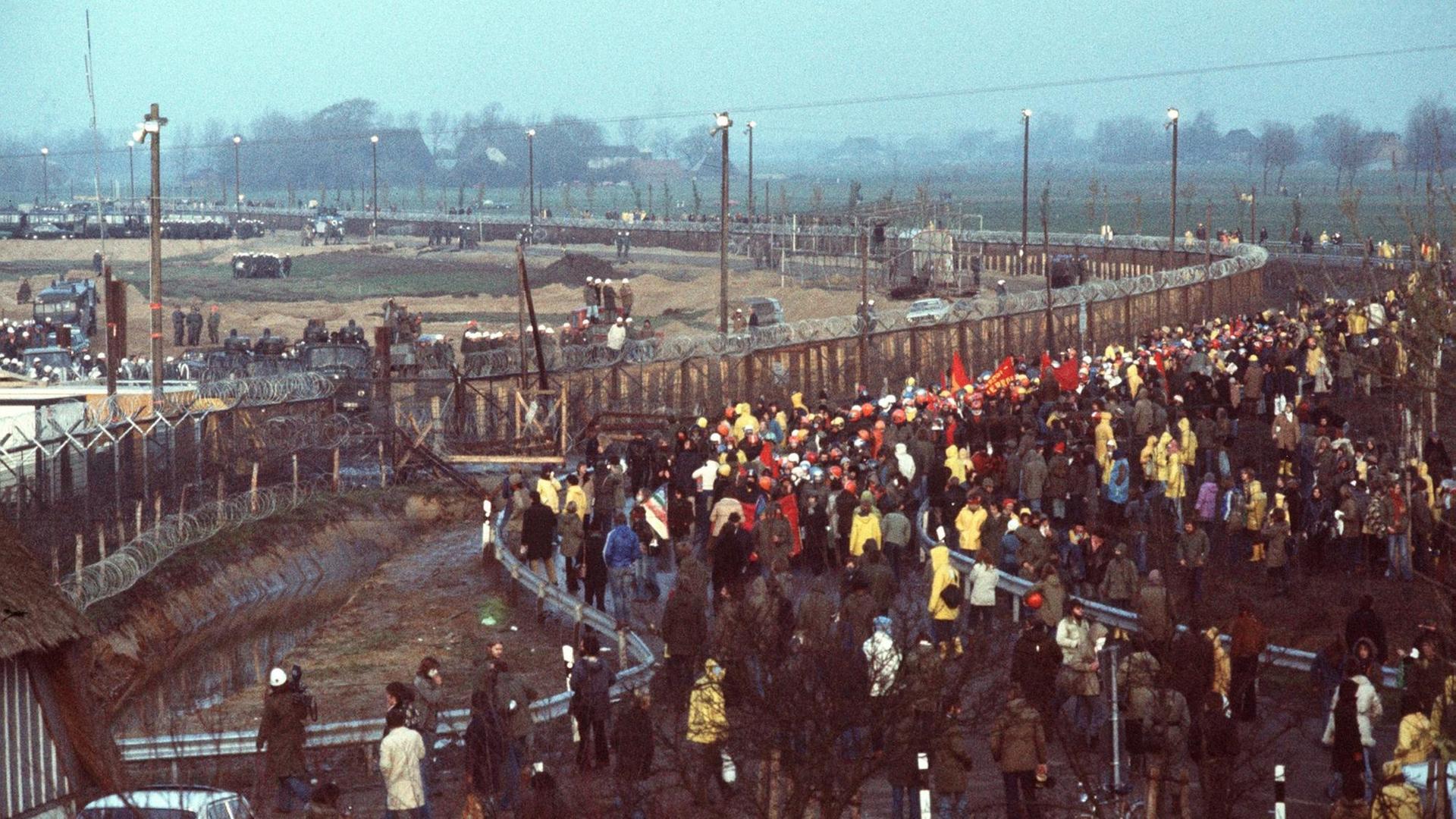 Demonstranten gegen den Kernkraftwerksbau in Brokdorf stehen mit Transparenten vor dem Baugelände, das mit Stacheldrahtzaun und Polizeiaufgebot abgesichert ist. Aufgenommen am 13. November 1976. Demonstranten gegen den Kernkraftwerksbau in Brokdorf stehen mit Transparenten vor dem Baugelände, das mit Stacheldrahtzaun und Polizeiaufgebot abgesichert ist. Aufgenommen am 13. November 1976.