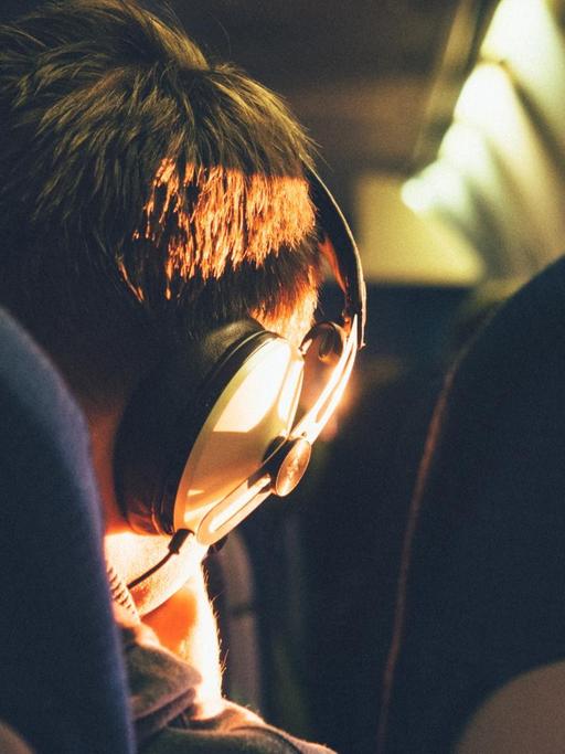 Das Bild zeigt den Hinterkopf eines Menschen mit Kopfhörern in einem Zugabteil, der bestimmt Podcasts hört.