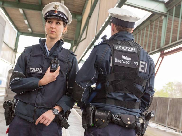 Zwei Polizisten präsentieren die neuen Bodycams: mit einem Monitor auf der Brust, einer Kamera auf der Schulter und dem Schriftzug "Videoüberwachung" auf dem Rücken