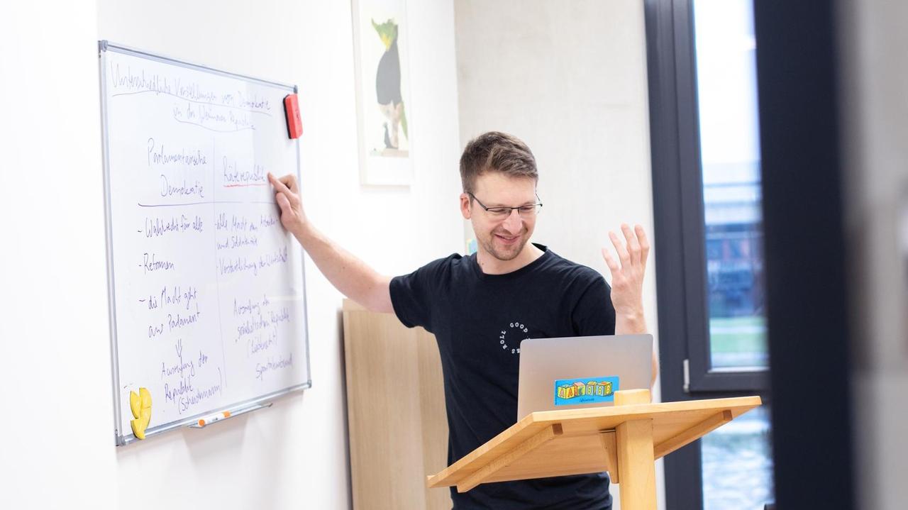 Ein Lehrer an einem Whiteboard in einen aufgeklappten Computer sprechend. Ein Lehrer an einem Whiteboard in einen aufgeklappten Computer sprechend.