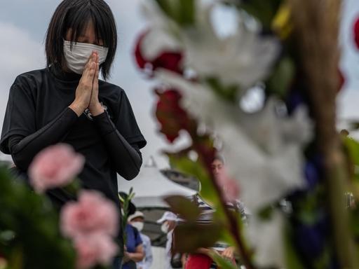 Eine Frau mit Mundschutz betet zwischen Blumen