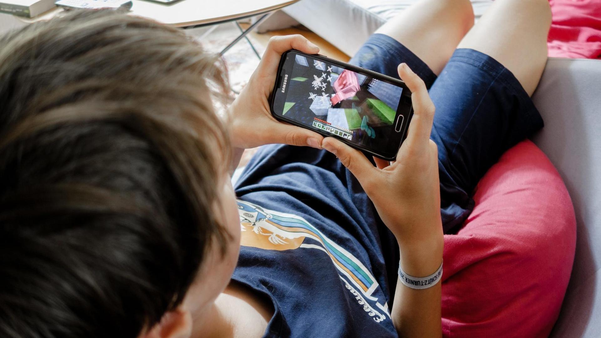 Eine Junge spielt am 10.08.2017 in Hamburg ein Spiel auf einem Smartphone. Foto: Markus Scholz | Verwendung weltweit