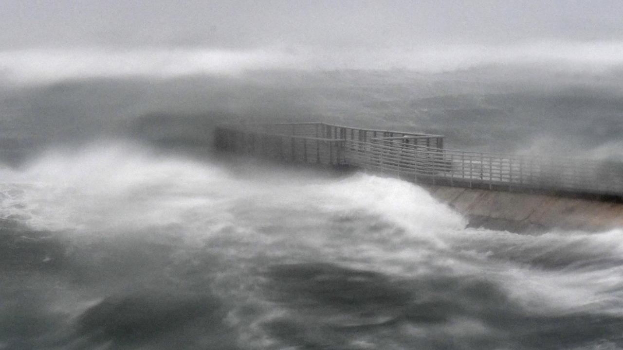 Das leicht unscharfe Bild zeigt ein von Wellen umtostes Pier mit einem Geländer.