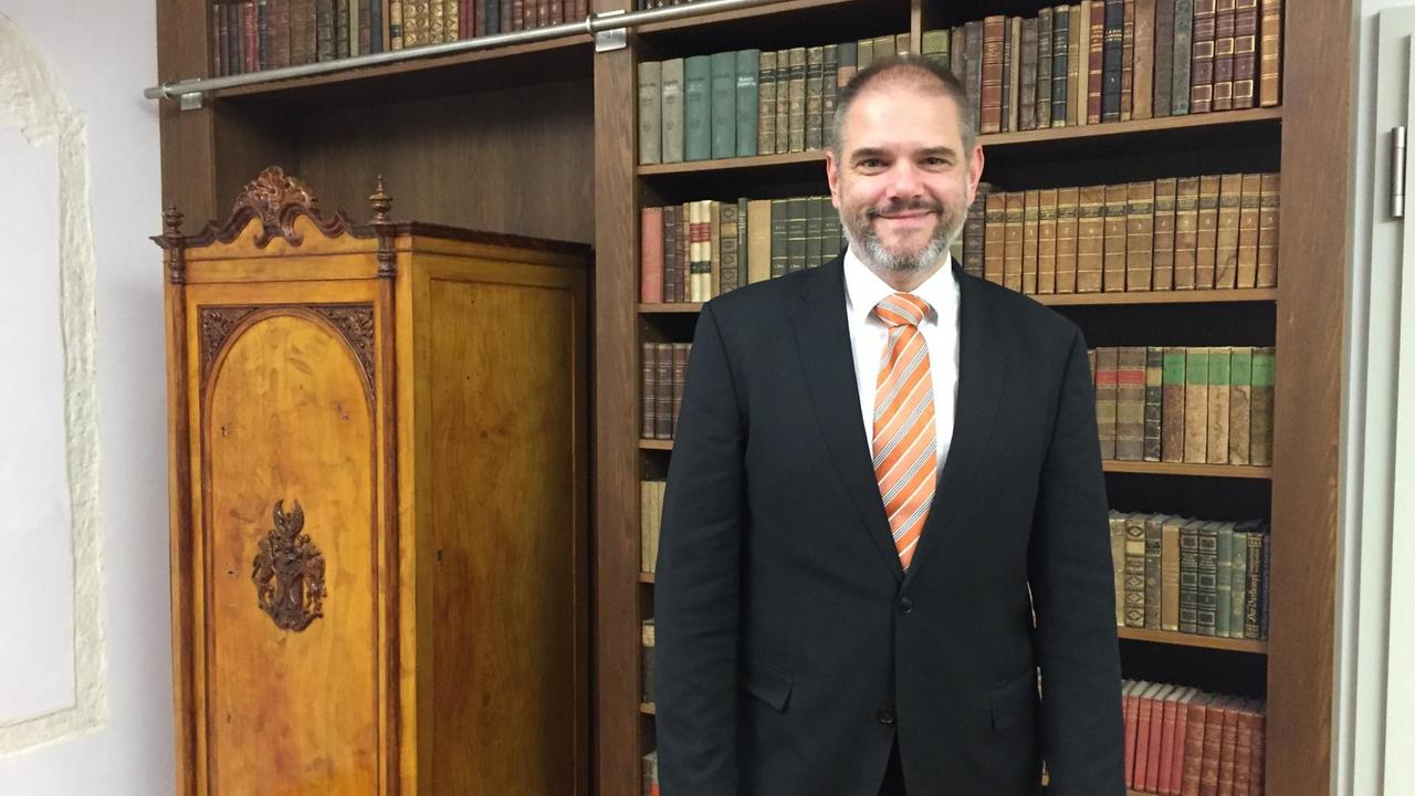 Porträt von Alexander Badrow vor einer Bücherwand. Porträt von Alexander Badrow vor einer Bücherwand.