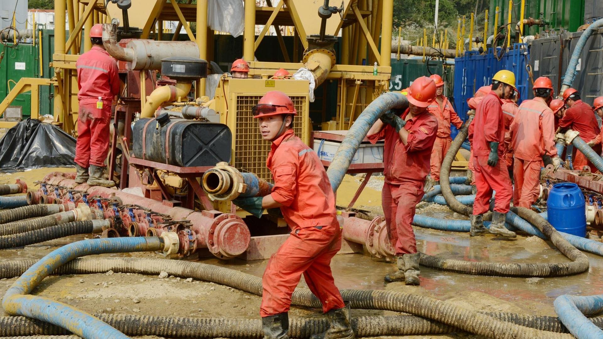 Chinesische Arbeiter in roten Overalls tragen armdicke Rohre für eine Schiefergasanlage durch den Matsch in Zentralchina. Chinesische Arbeiter in roten Overalls tragen armdicke Rohre für eine Schiefergasanlage durch den Matsch in Zentralchina.