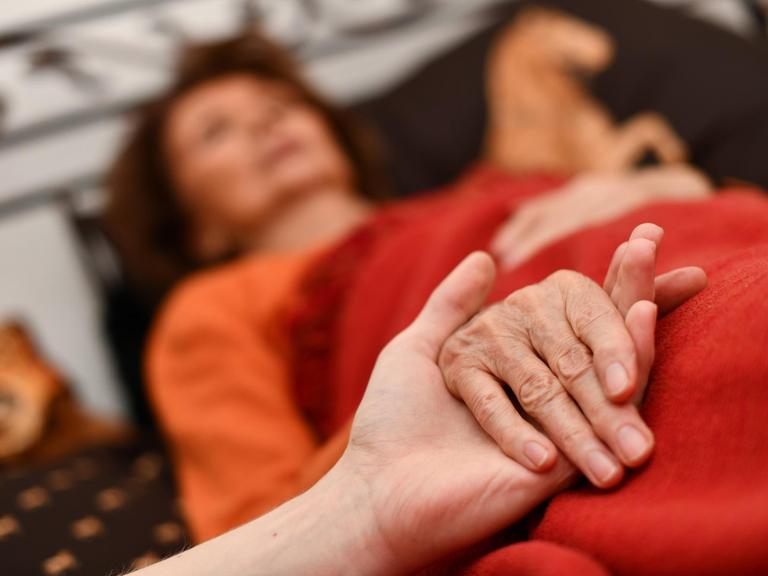 Alter Frau, die im Bett liegt, werden die Hände gehalten