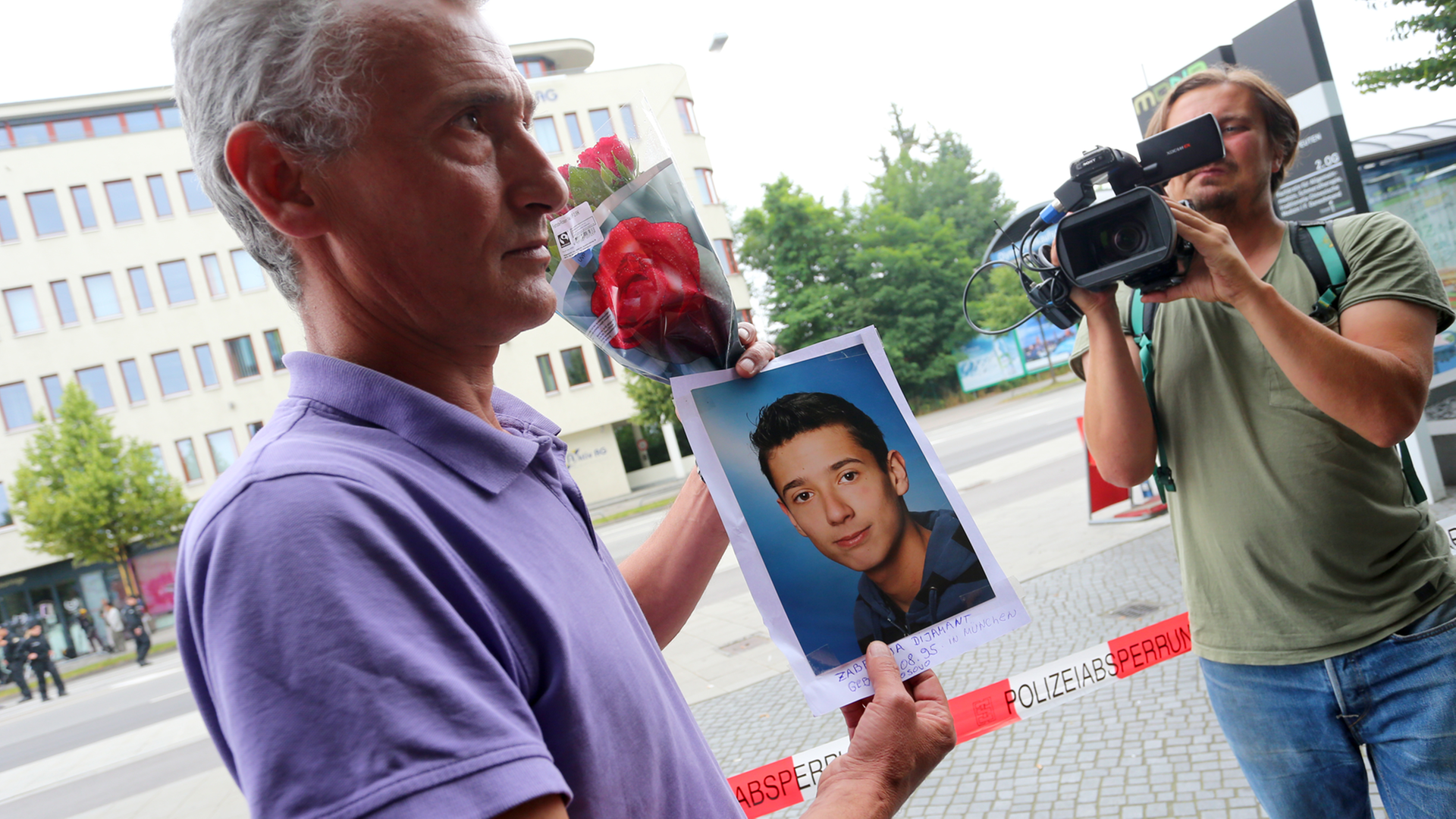 Naim Zabergja steht mit einem Foto seines getöteten Sohnes Dijamant am 23.07.2016 vor Medienvertretern am Olympia-Einkaufszentrum in München (Bayern), das die Polizei nach einer Schießerei mit Toten und Verletzten am Vortag abgesperrt hat. Naim Zabergja steht mit einem Foto seines getöteten Sohnes Dijamant am 23.07.2016 vor Medienvertretern am Olympia-Einkaufszentrum in München (Bayern), das die Polizei nach einer Schießerei mit Toten und Verletzten am Vortag abgesperrt hat.