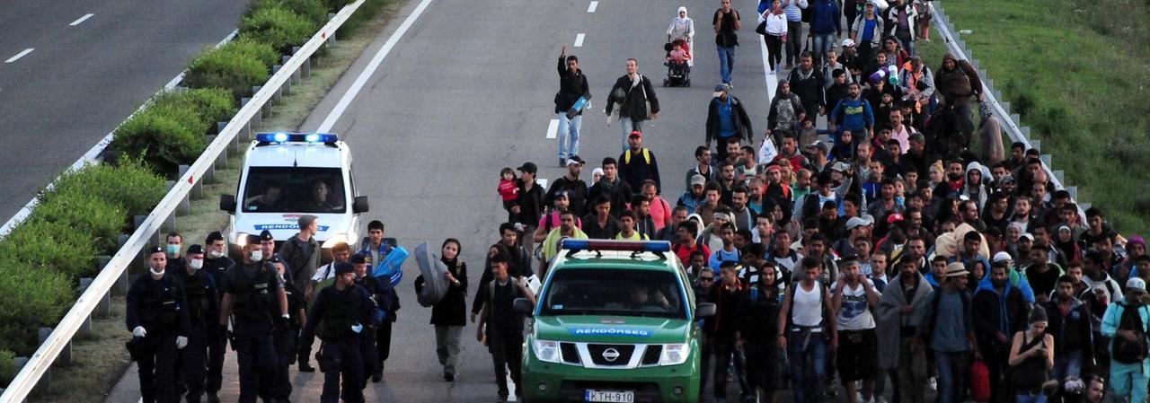 Begleitet von einem Polizeiauto sind zahlreiche Menschen zu Fuß auf der Autobahn unterwegs. Begleitet von einem Polizeiauto sind zahlreiche Menschen zu Fuß auf der Autobahn unterwegs.