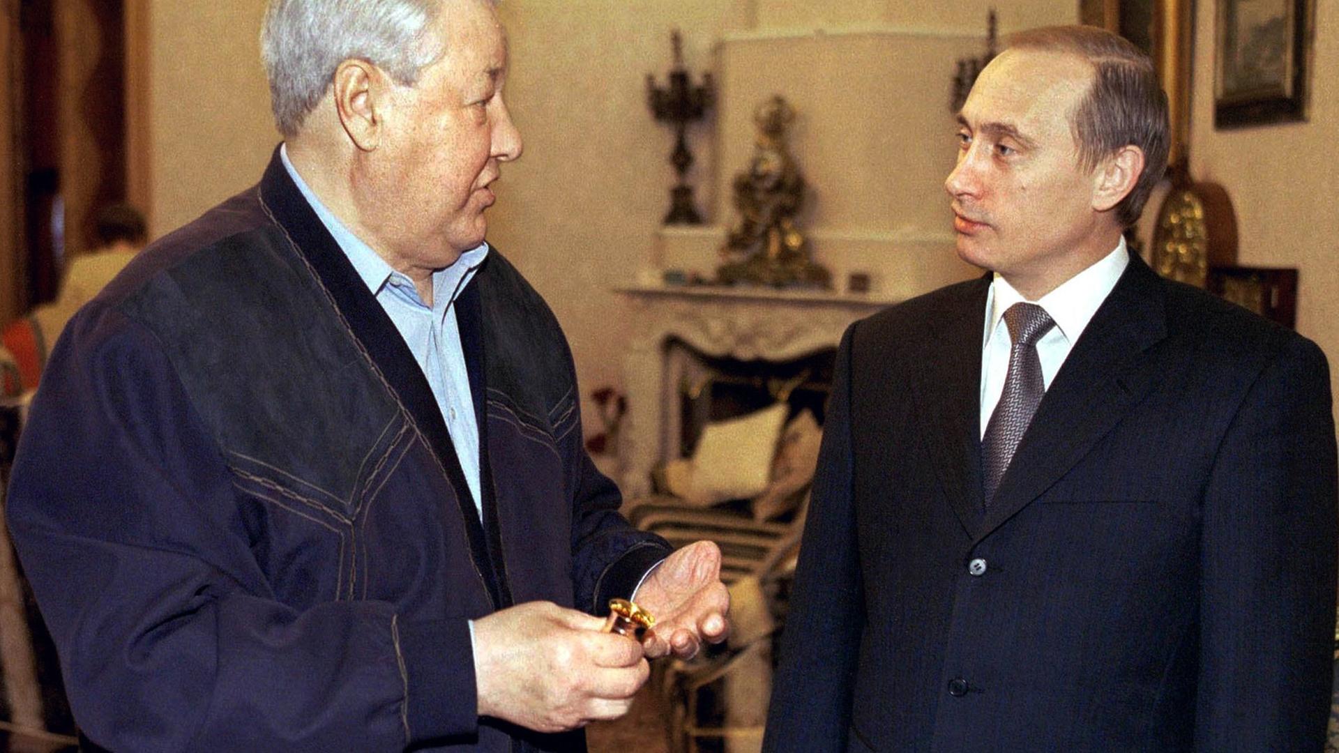 Präsident Putin steht rechts in einem noblen Innenraum udn schaut den älteren Boris Jelzin von der Seite erwartungsfroh an. Präsident Putin steht rechts in einem noblen Innenraum udn schaut den älteren Boris Jelzin von der Seite erwartungsfroh an.