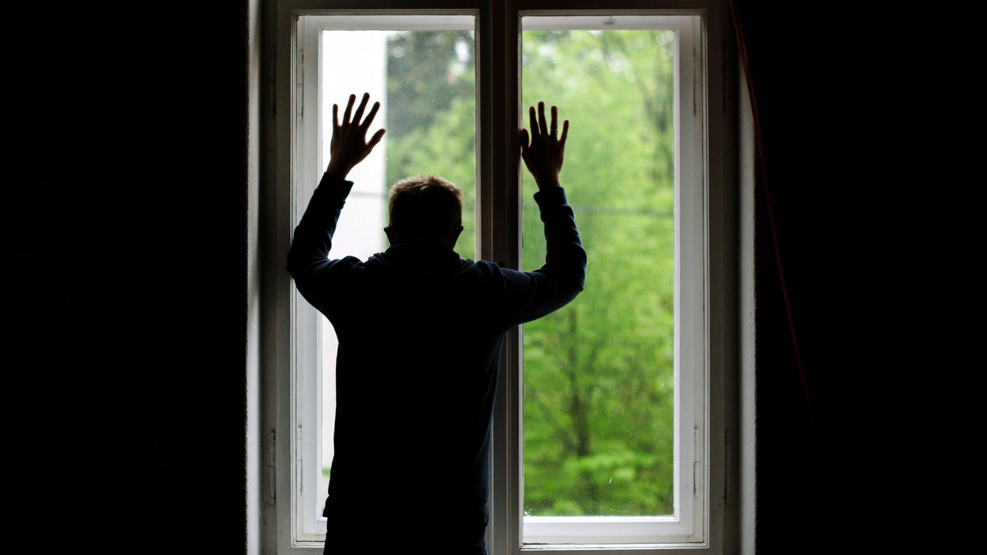 Ein Mann steht allein an einem Fenster und schaut nach draußen. Ein Mann steht allein an einem Fenster und schaut nach draußen.