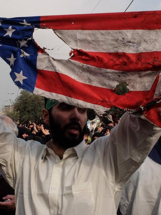 Ein Mann hält bei Protesten in der iranischen Hauptstadt Tehran eine verannte Fahne der USA hoch.