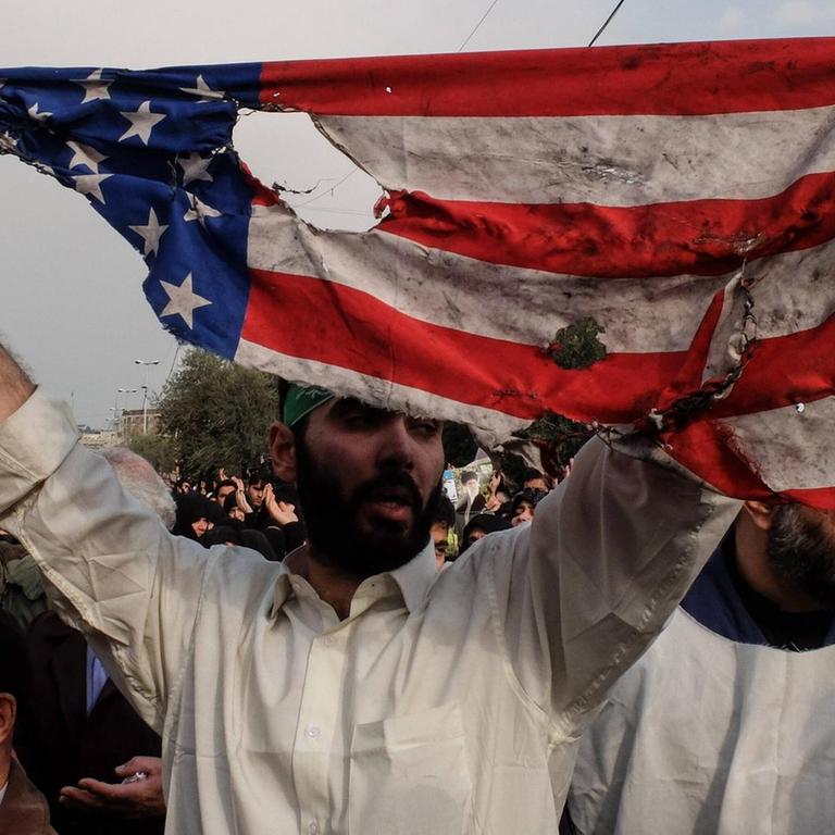 Ein Mann hält bei Protesten in der iranischen Hauptstadt Tehran eine verannte Fahne der USA hoch.