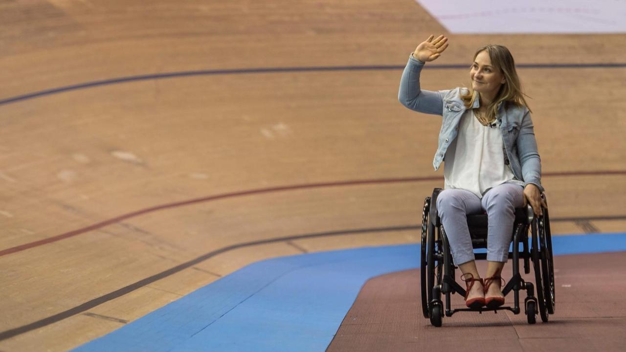 Ex-Bahnradsportlerin Kristina Vogel beim Weltcup 2018 winkend im Rollstuhl auf der Rennbahn Ex-Bahnradsportlerin Kristina Vogel beim Weltcup 2018 winkend im Rollstuhl auf der Rennbahn