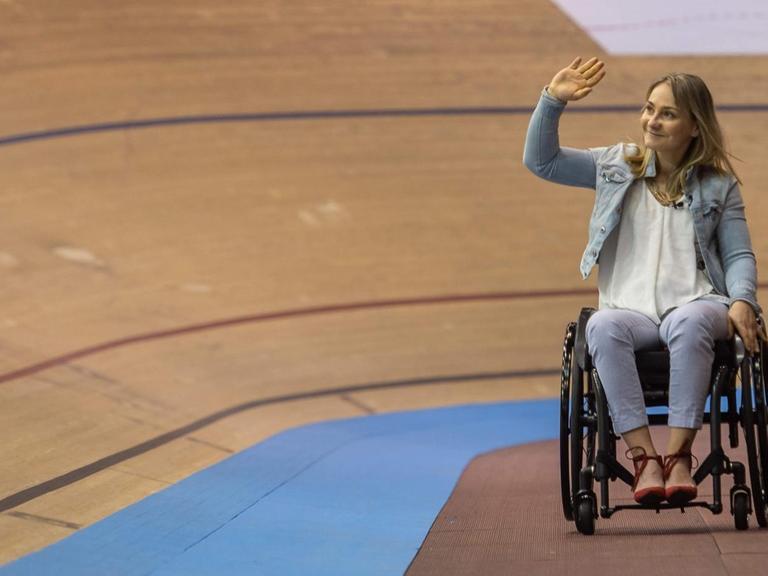Ex-Bahnradsportlerin Kristina Vogel beim Weltcup 2018 winkend im Rollstuhl auf der Rennbahn