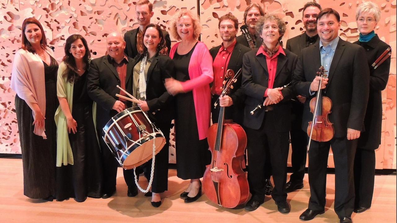 Die Musikerinnen und Musiker der Boston Camerata stehen in einer Zweier-Reihe zusammen und schauen in die Kamera, einige Instrumente wie Trommel, Violoncello, Geige und Flöte sind zu sehen Die Musikerinnen und Musiker der Boston Camerata stehen in einer Zweier-Reihe zusammen und schauen in die Kamera, einige Instrumente wie Trommel, Violoncello, Geige und Flöte sind zu sehen