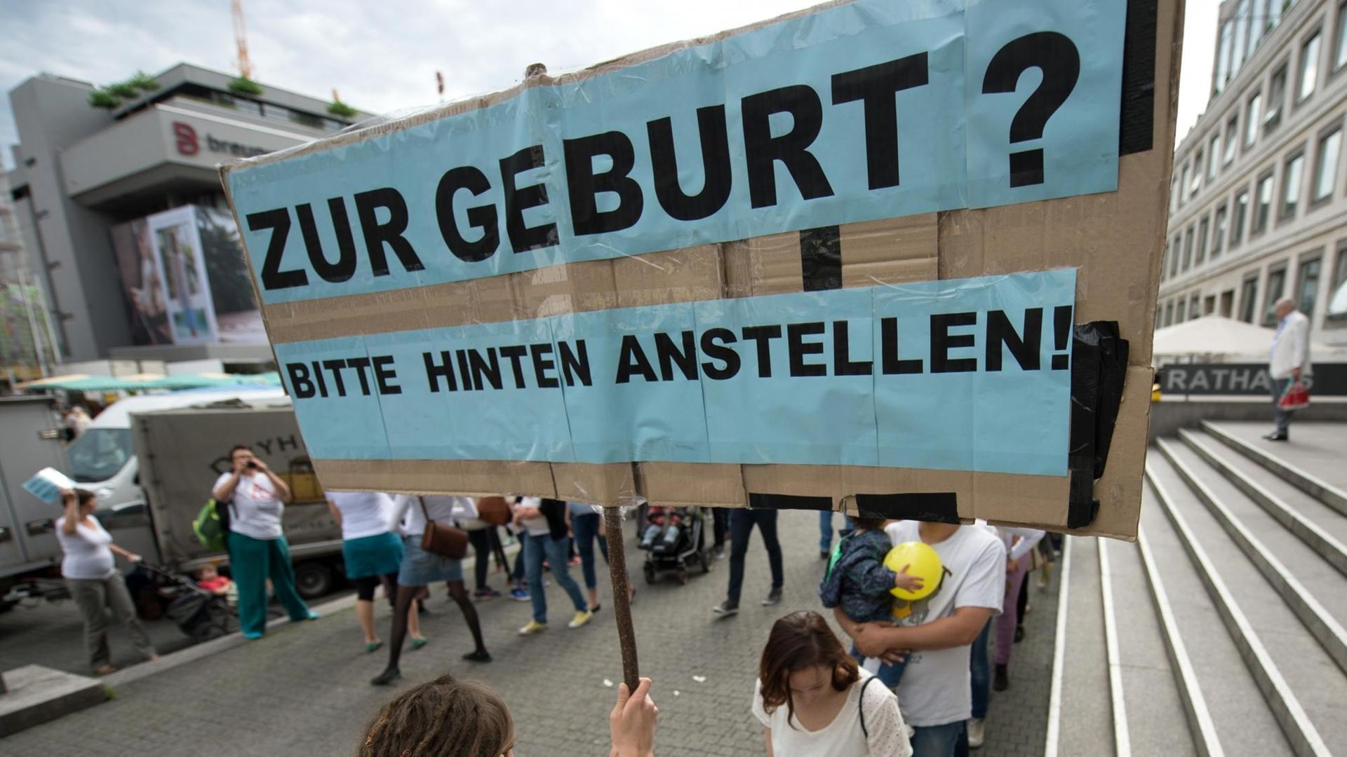 Eine Hebamme hält in Stuttgart (Baden-Württemberg) ein Schild hoch mit der Aufschrift "Zur Geburt? Bitte hinten anstellen!" Rund 50 Hebammen protestierten mit einem Flashmob für bessere Arbeitsbedingungen. Eine Hebamme hält in Stuttgart (Baden-Württemberg) ein Schild hoch mit der Aufschrift "Zur Geburt? Bitte hinten anstellen!" Rund 50 Hebammen protestierten mit einem Flashmob für bessere Arbeitsbedingungen.