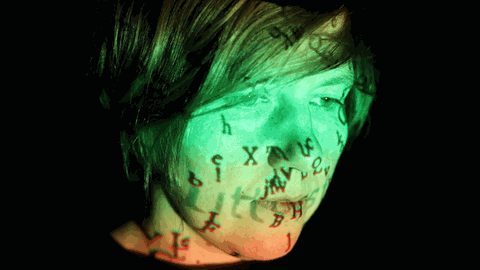 Projektionen spiegeln sich auf der Oberfläche des Gesichts von der Künstlerin Masha Qrella. In "Woanders" vertont Masha Qrella Texte von Thomas Brasch.