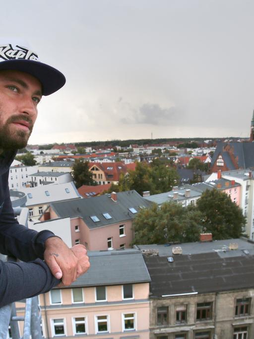 Der Rapper Marteria steht auf dem Dach der Brauerei in Rostock vor der Silhouette der Kröpeliner Tor Vorstadt