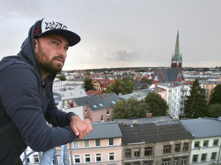 Der Rapper Marteria steht auf dem Dach der Brauerei in Rostock vor der Silhouette der Kröpeliner Tor Vorstadt