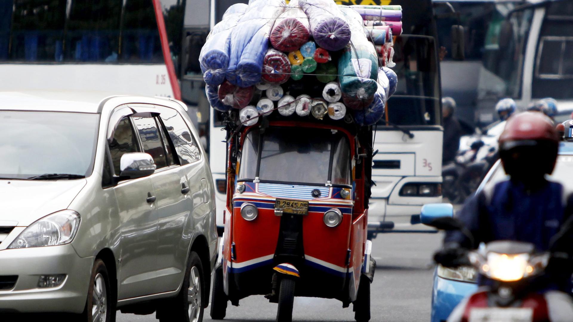 Ein überladenes Taxi, Bajaj genannt, zwischen Autos, Bussen und Mopedfahrern in Jakarta Ein überladenes Taxi, Bajaj genannt, zwischen Autos, Bussen und Mopedfahrern in Jakarta