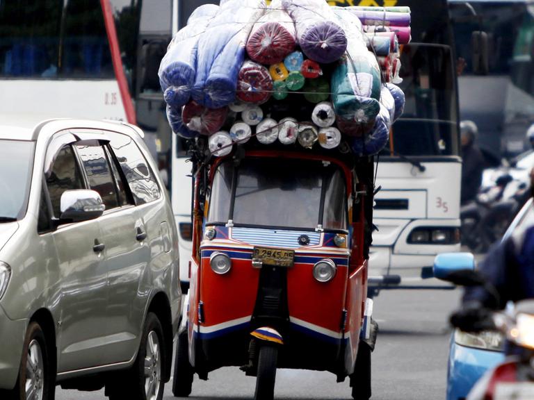 Ein überladenes Taxi, Bajaj genannt, zwischen Autos, Bussen und Mopedfahrern in Jakarta