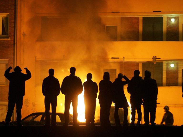 Vor zehn Jahren in Clichy-sous-Bois: Jugendliche stehen vor einem brennenden Auto. Man sieht nur ihre Schatten.