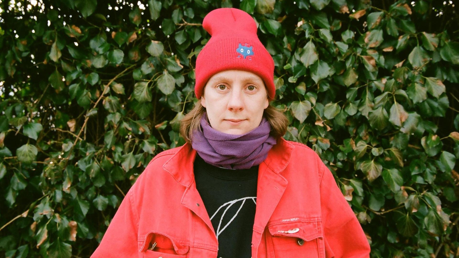 Autorin Anna Haifisch mit einer roten Jacke und roter Wintermütze vor Efeu, guckt direkt in die Kamera Autorin Anna Haifisch mit einer roten Jacke und roter Wintermütze vor Efeu, guckt direkt in die Kamera