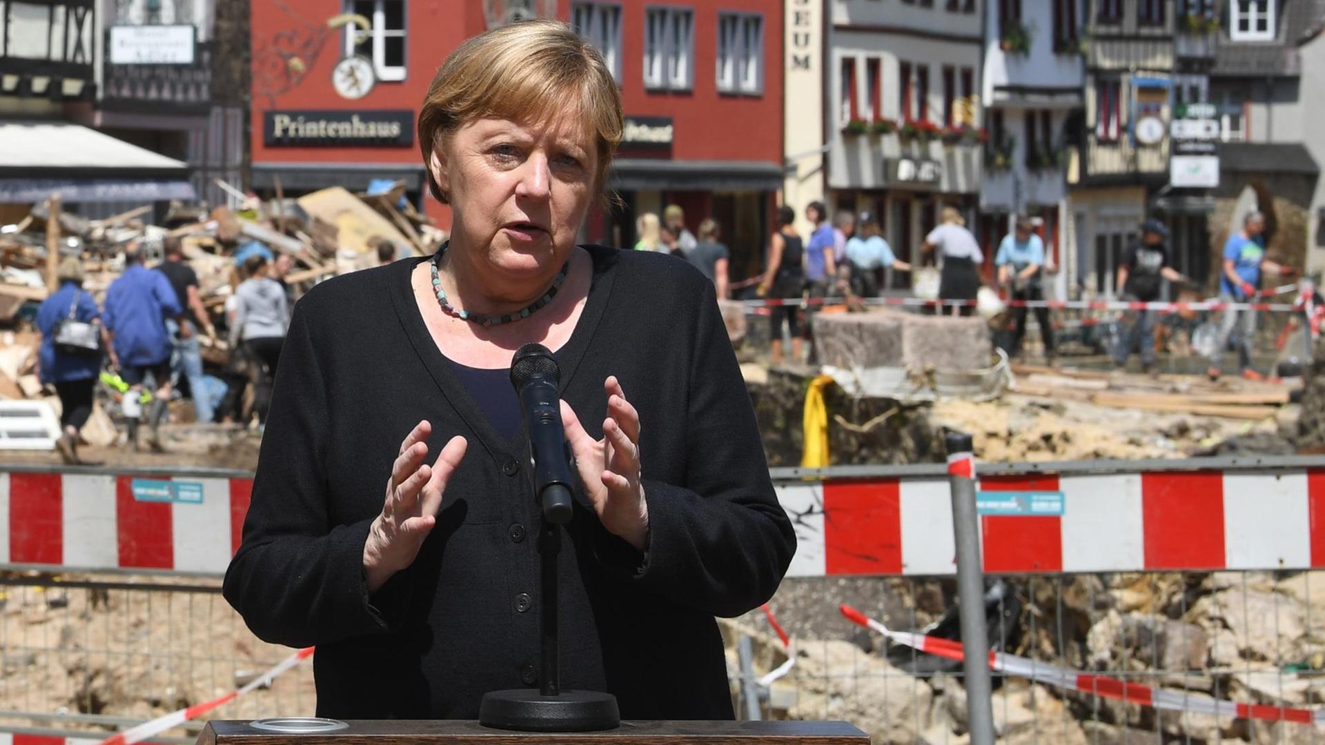 Bundes-Kanzlerin Angela Merkel steht in der Stadt Münstereifel. Hinter ihr sind die Schäden von dem Hoch-Wasser zu erkennen. 