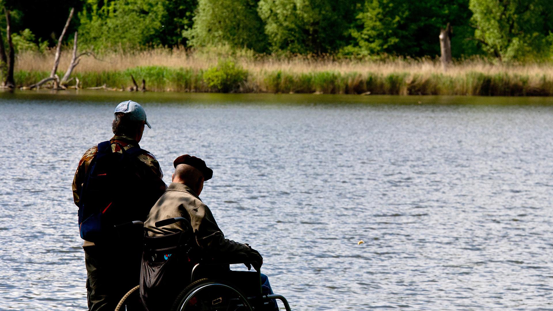 Ein Mann begleitet am 07.05.2014 einen älteren Herren in einem Rollstuhl um den Malchower See in Berlin. Ein Mann begleitet am 07.05.2014 einen älteren Herren in einem Rollstuhl um den Malchower See in Berlin.