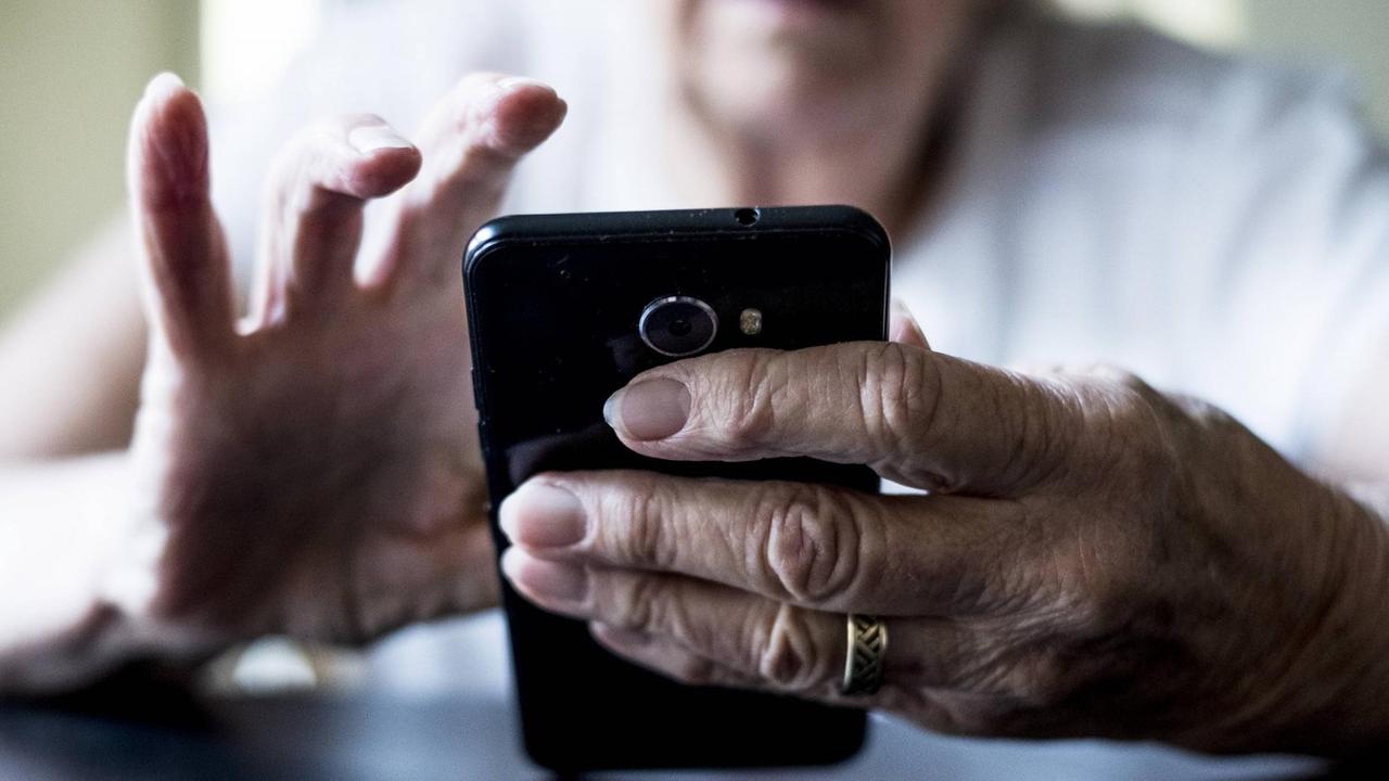 Eine Seniorin hält ein Smartphone in der Hand. Eine Seniorin hält ein Smartphone in der Hand.