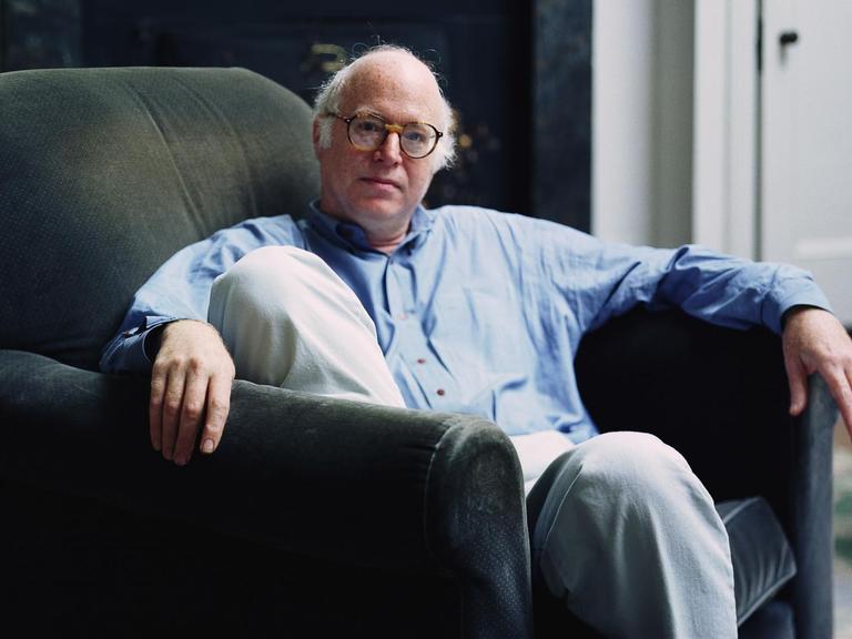 Auf dem Bild ist der Soziologe Richard Sennett zu sehen. Er sitzt in einem bequemen Stuhl und trägt ein blaues Jeanshemd