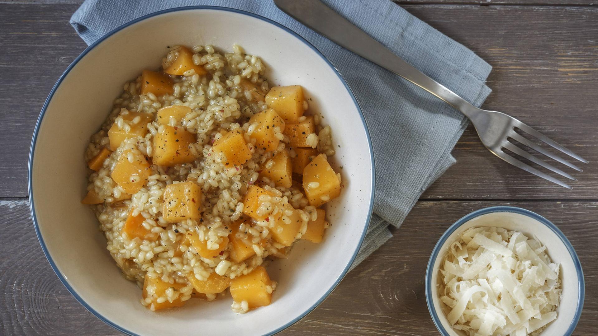 Eine Schüssel mit Rüben-Risotto, daneben eine kleine Schale geriebener Parmesan Eine Schüssel mit Rüben-Risotto, daneben eine kleine Schale geriebener Parmesan