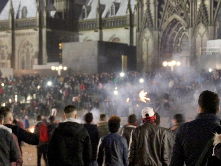 Menschengruppen vor der Kulisse des Kölner Doms, dazwischen Rauchschwaden.
