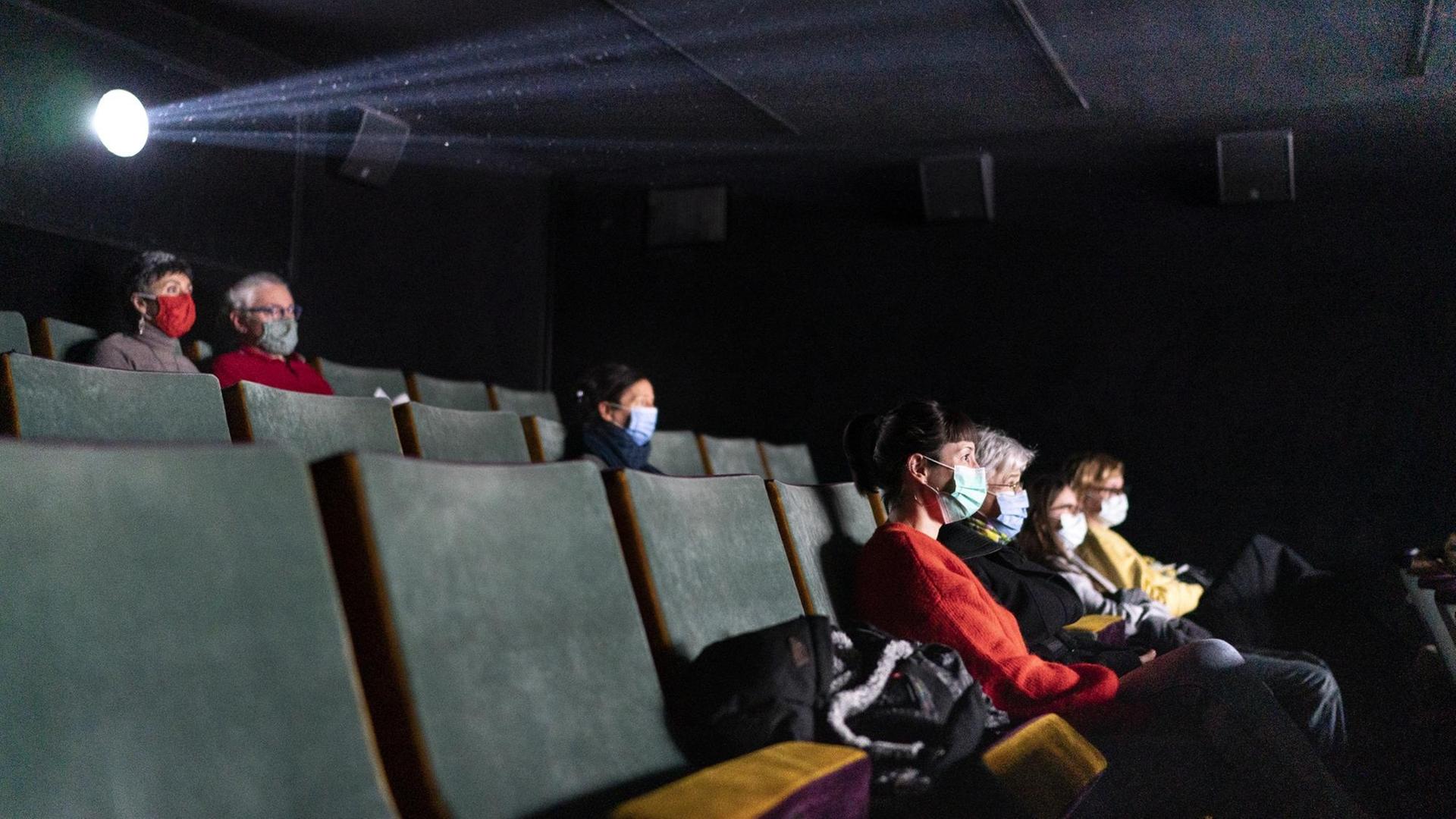 Personen sitzen mit Abstand und Maske in einem Kino.