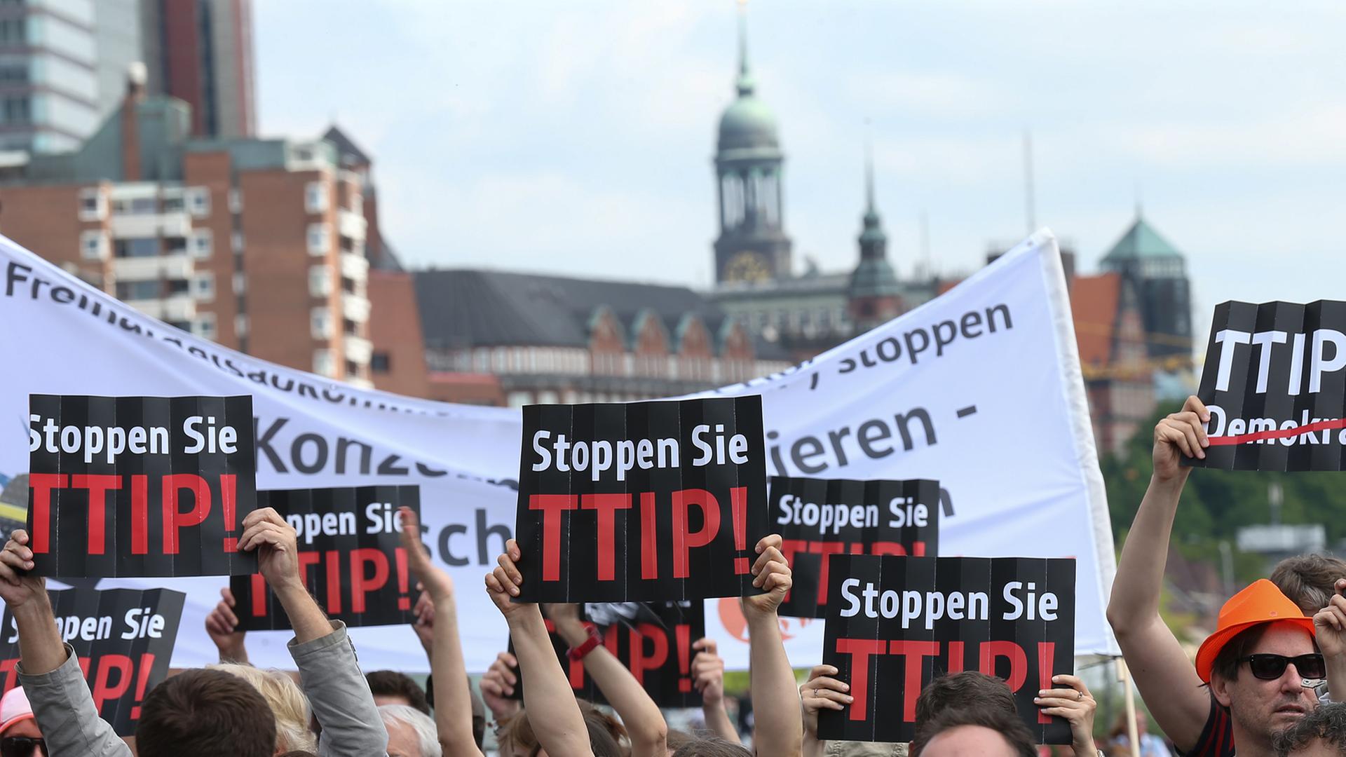 Demonstranten halten am 17.05.2014 in Hamburg bei einer Wahlkampfveranstaltung der CDU auf dem Hamburger Fischmarkt ein Plakat mit der Aufschrift "Stoppen Sie TTIP" in die Höhe. Demonstranten halten am 17.05.2014 in Hamburg bei einer Wahlkampfveranstaltung der CDU auf dem Hamburger Fischmarkt ein Plakat mit der Aufschrift "Stoppen Sie TTIP" in die Höhe.