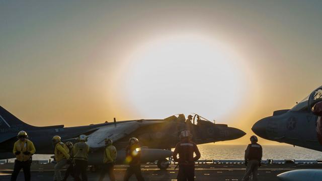 Ein Kampfflugzeug auf einem Flugzeugträger im Sonnenuntergang.