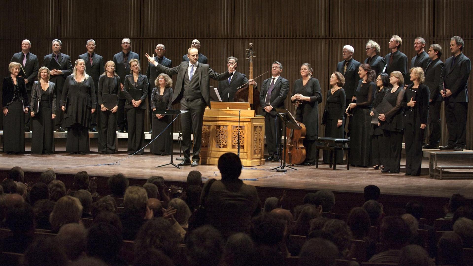 Der Nederlands Kamerkoor feierte mit seinem Dirigenten Peter Dijkstra das Jubiläumskonzert zum 75-jährigen Bestehen im Muziekgebouw in Amsterdam. Der Chor trägt schwarze Konzertkleidung, der Dirigent steht in der Mitte vor einer Truhenorgel und dem Continuo-Ensemble. Der Nederlands Kamerkoor feierte mit seinem Dirigenten Peter Dijkstra das Jubiläumskonzert zum 75-jährigen Bestehen im Muziekgebouw in Amsterdam. Der Chor trägt schwarze Konzertkleidung, der Dirigent steht in der Mitte vor einer Truhenorgel und dem Continuo-Ensemble.