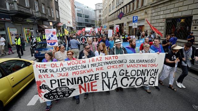 In Warschau demonstrieren Menschen am Samstag gegen den Nato-Gipfel. Sieht halten ein Schild mit der Aufschrift: "Geld gegen den Hunger, nicht für Panzer"