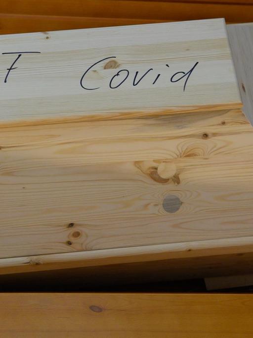 "Covid" steht auf einem Sarg mit einem Verstorbenen, der an oder mit dem Coronavirus gestorben ist. Die Särge stehen vor der Einäscherung im Andachtsraum im Krematorium.
