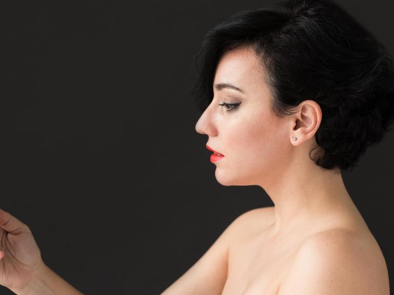 Ein Frau mit nackten Schultern macht ein Selfie von sich. Der Hintergrund ist schwarz.