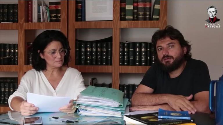 Frau und junger Mann mit Vollbart im Büro vor Bücherregal am Schreibtisch mit dicken Akten. Frau und junger Mann mit Vollbart im Büro vor Bücherregal am Schreibtisch mit dicken Akten.